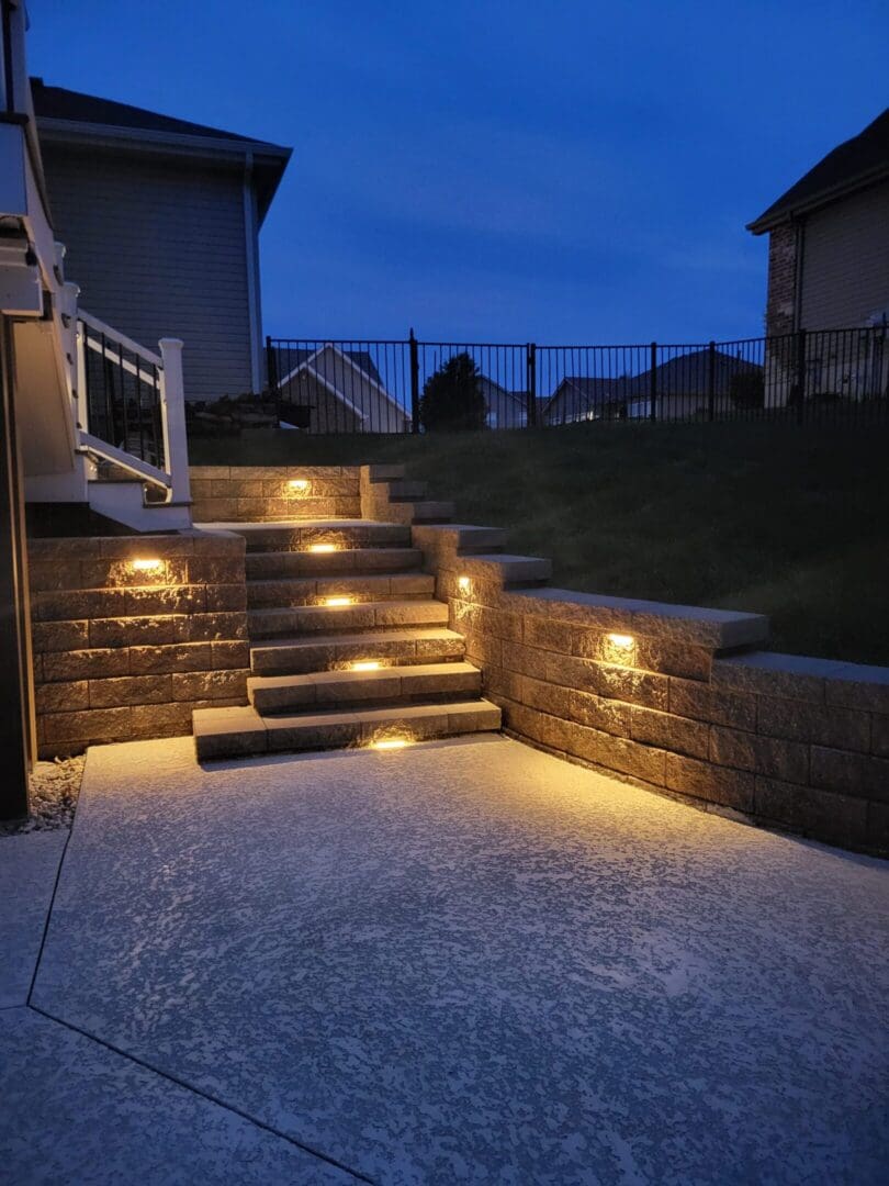 Outdoor stairs and retaining wall illuminated by warm lights at dusk.
