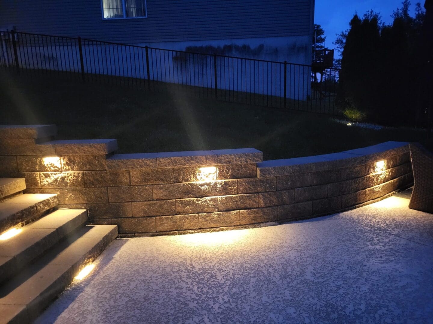 Outdoor stone wall with built-in lighting illuminating a patio area at night.