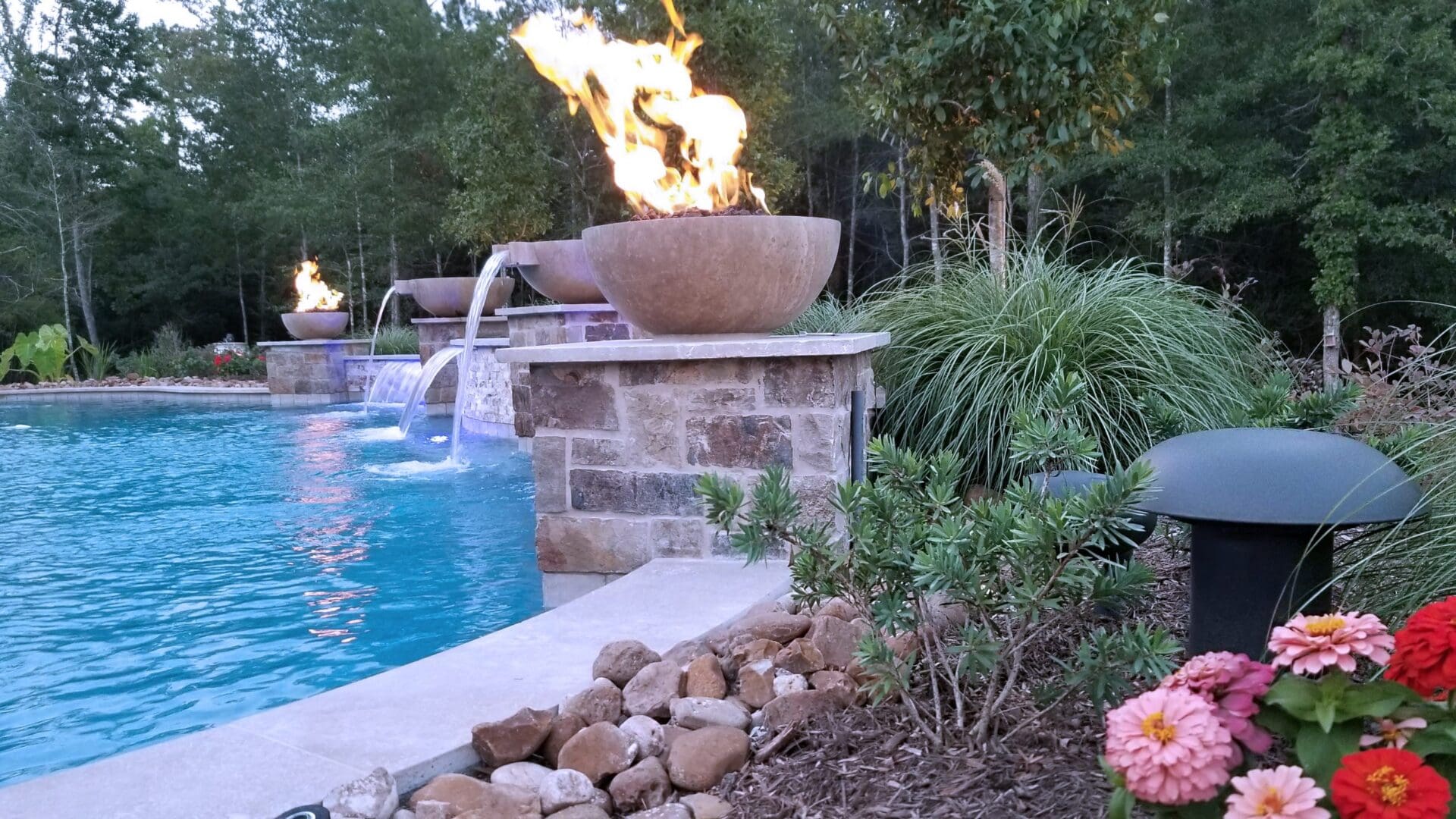 A poolside fire bowl with water features and surrounding greenery.